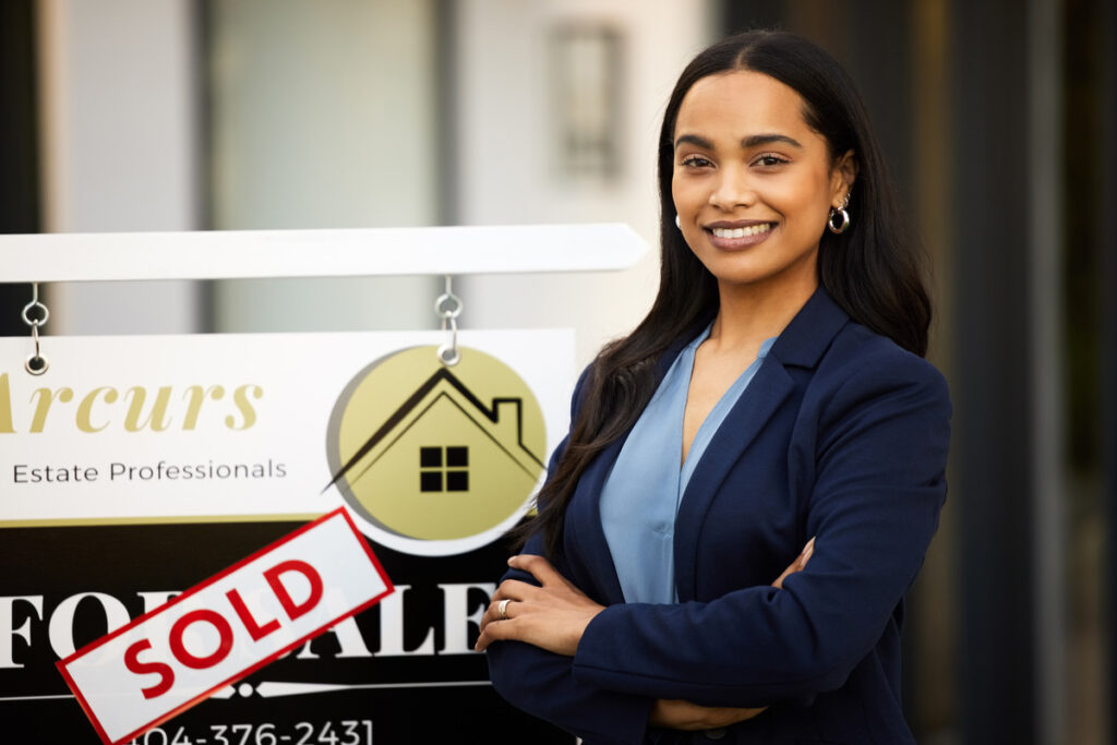 Licensed real estate salesperson standing in front of sold sign.